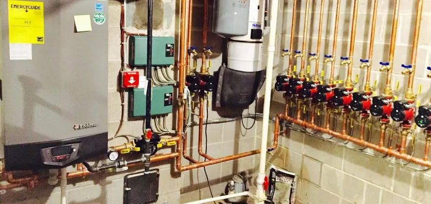 A wall-hung boiler beside a row of red circulator pumps on a copper zone manifold
